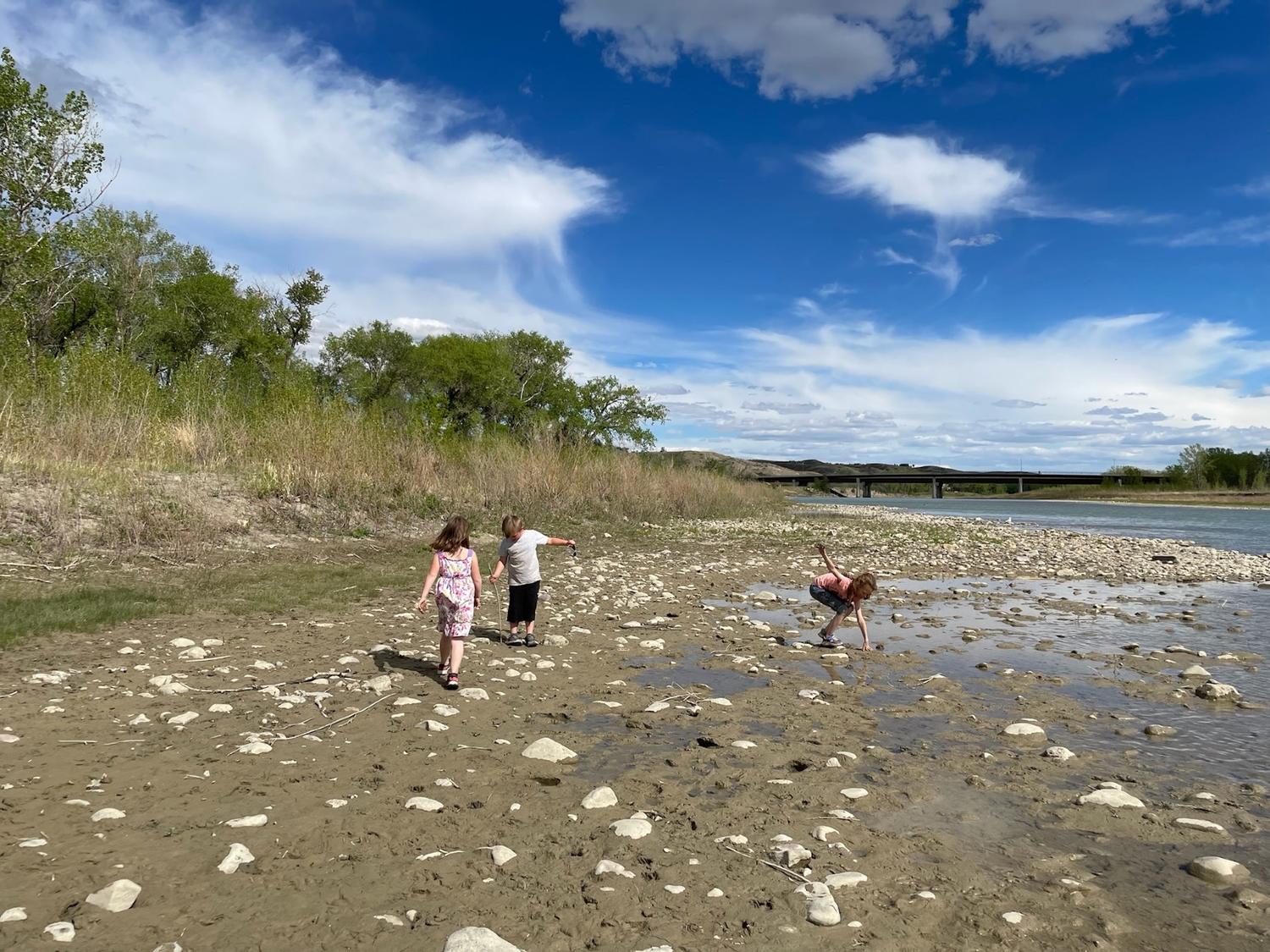 Children exploring a rocky river shore under a big blue sky